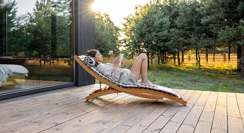 Frau liegt bei Sonnenuntergang auf einem Liegestuhl auf ihrer Terrasse und liest ein Buch