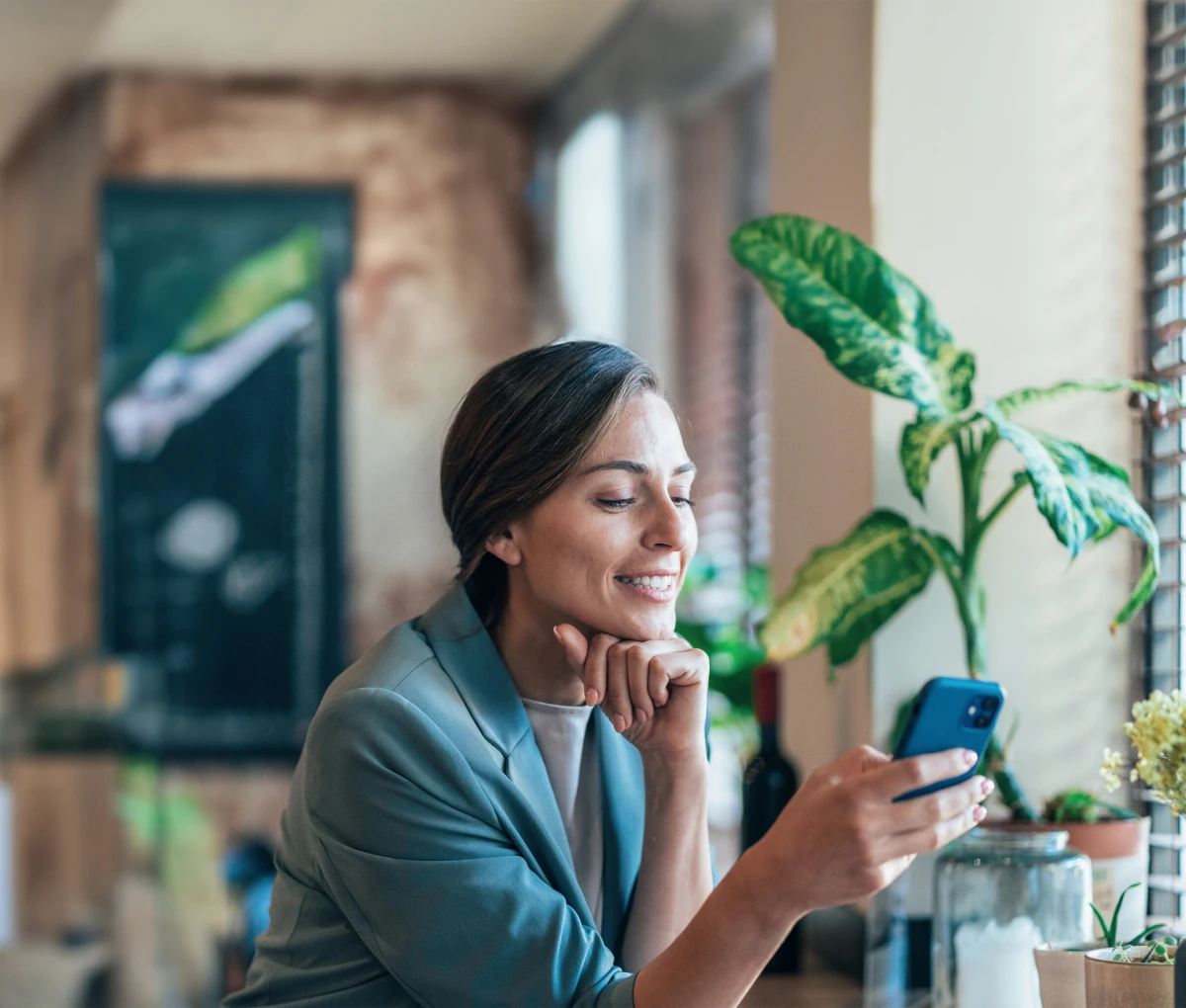 Grauhaarige Frau in grauem Blazer sitzt in einem Café und schaut in ihr Smartphone
