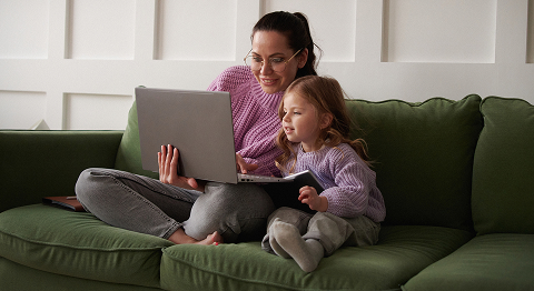 Mutter und Tochter sitzen auf Sofa und schauen auf einen Laptop