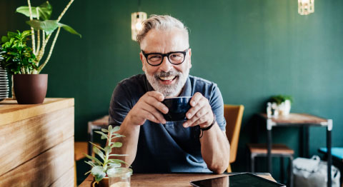 Mann mit Brille und Kaffe in der Hand lächelt
