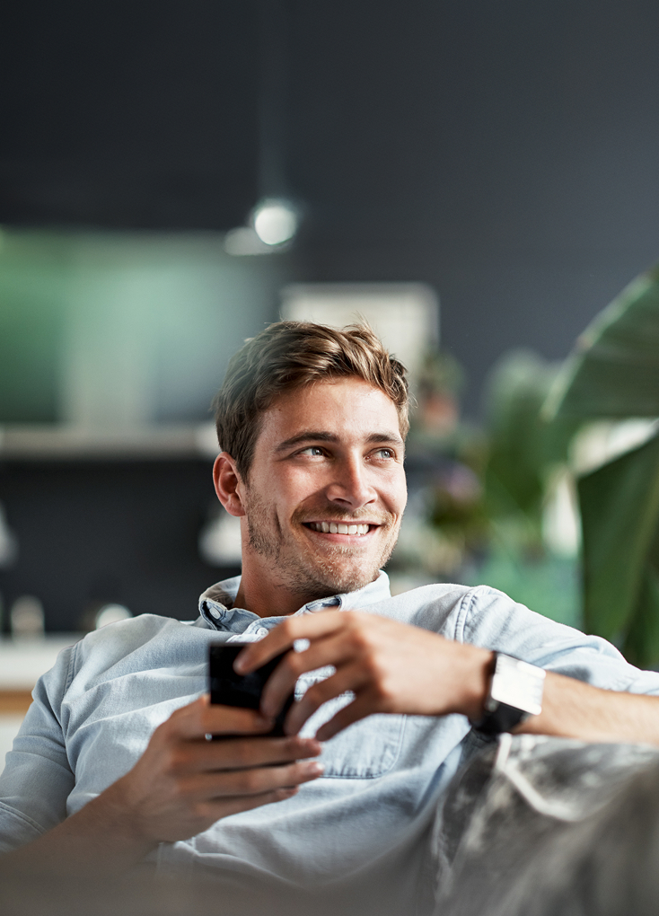 Mann in hellblauem Hemd hält ein Handy und lächelt.