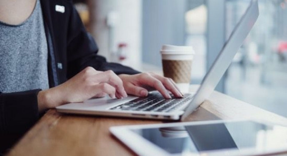 Nahaufnahme einer Person, die am Laptop tippt und Kaffee trinkt