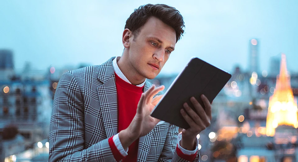 Mann in rotem Pullover und kariertem Sakko tippt in sein Tablet