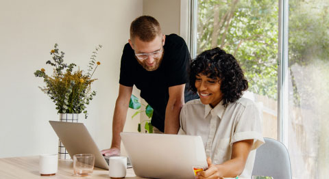 Mann und Frau sind im Wohnzimmer und arbeiten an zwei Laptops