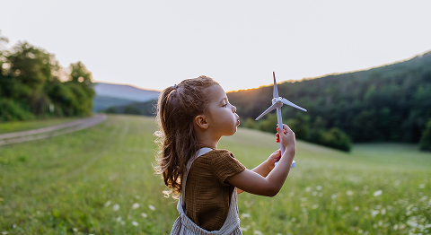 Mädchen pustet auf ein Windrad in der Hand