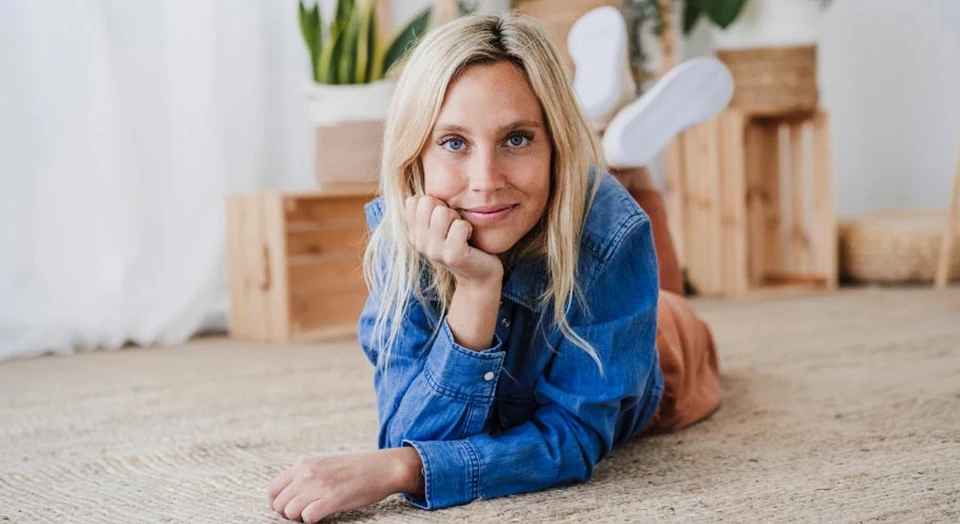 Blonde Frau in Jeansjacke liegt auf dem Bauch auf dem Boden und schaut in die Kamera