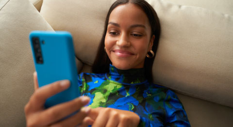 Frau auf dem Sofa am blauen Smartphone mit buntem Oberteil