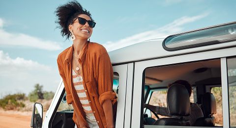 Frau mit Sonnenbrille und orangenem Hemd lehnt sich aus dem Fenster eines Jeeps