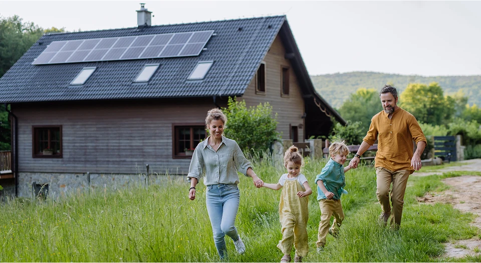 Familie mit zwei Kindern ist auf dem Feld vor ihrem Haus und hält sich an den Händen