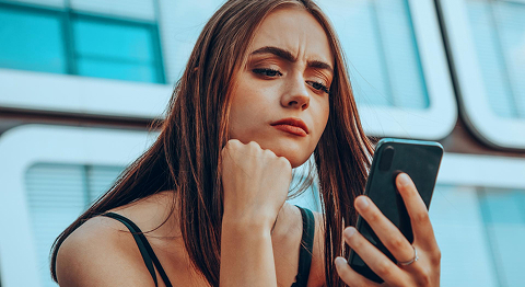 Frau sitzt draußen und schaut grübeln in ihr Smartphone