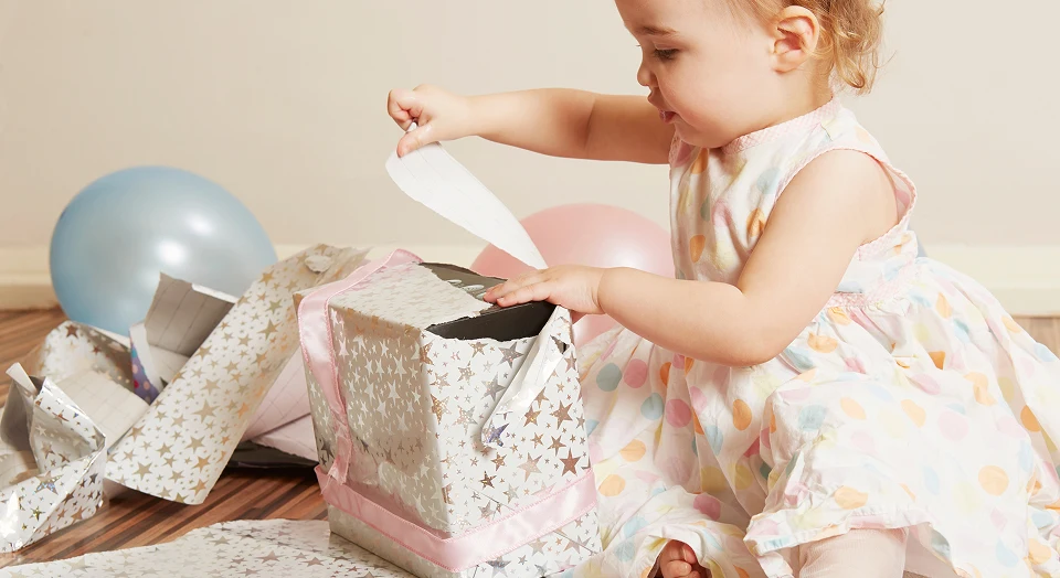 Baby packt Geburtstagsgeschenke neben bunten Luftballons aus