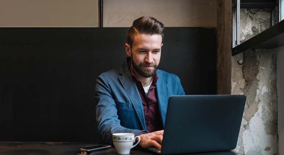 Mann mit dunklen Haaren sitzt auf einer Sitzbank an seinem Laptop