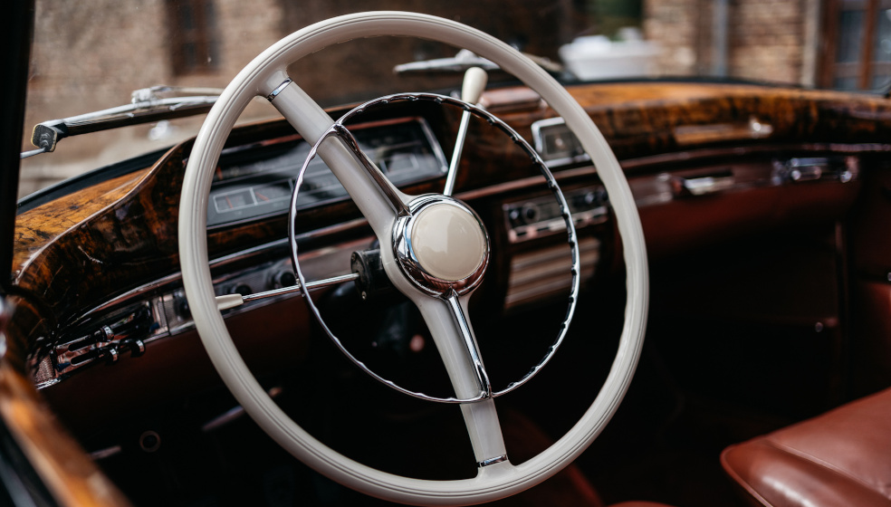 Nahaufnahme eines Oldtimer-Lenkrads mit Chromdetails im Innenraum eines klassischen Fahrzeugs.