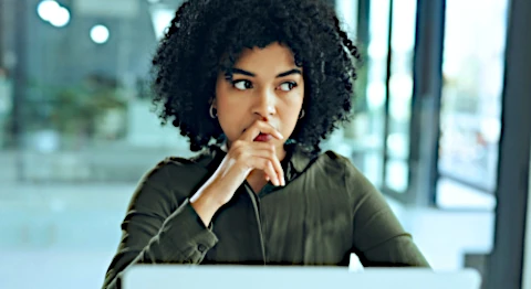 Frau mit Afro sitzt vor ihrem Notebook und blickt gedankenvoll  nach oben