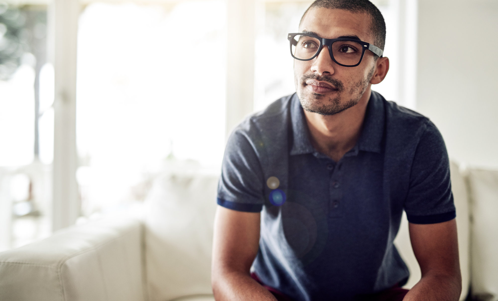 Eine Person mit dunklen Haaren, Brille und blauem Hemd blickt nachdenkllich lächelnd nach oben
