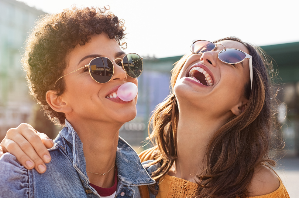 Zwei Frauen mit Sonnenbrille lachen glücklich und machen Kaugummiblasen