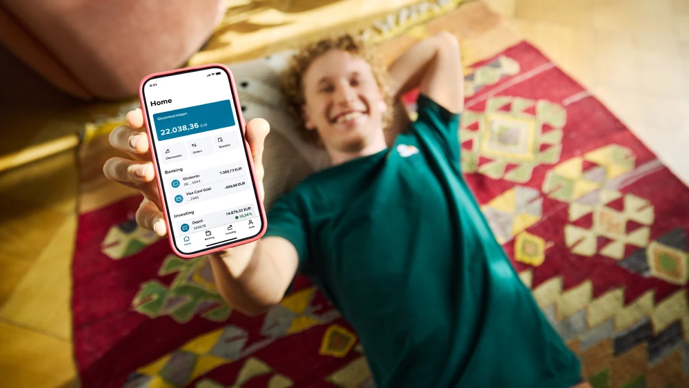 Junge in grünem T-Shirt liegt auf dem Boden und sein Smartphone mit geöffneter CB Neo App in die Kamera