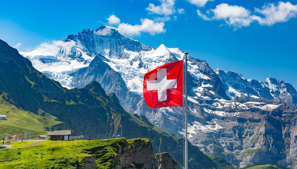 Rote Flagge mit weißem Kreuz der Schweiz vor beschneitem Gebirge