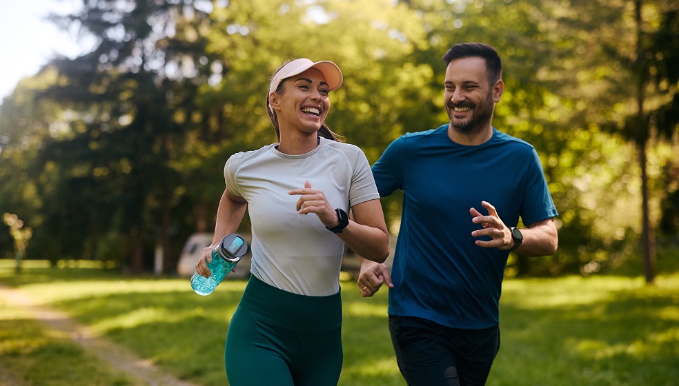 Frau und Mann gehen im Park joggen und lachen dabei