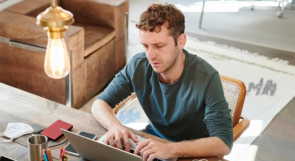Lockiger Mann sitzt am Schreibtisch und arbeitet an seinem Laptop