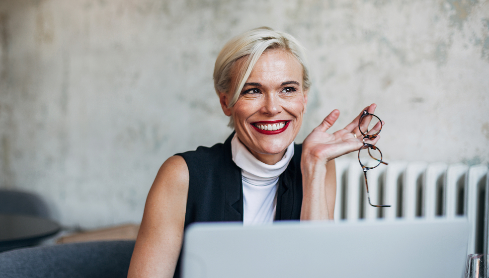 Blonde Frau sitzt in einem Café am Laptop und schaut in die Ferne
