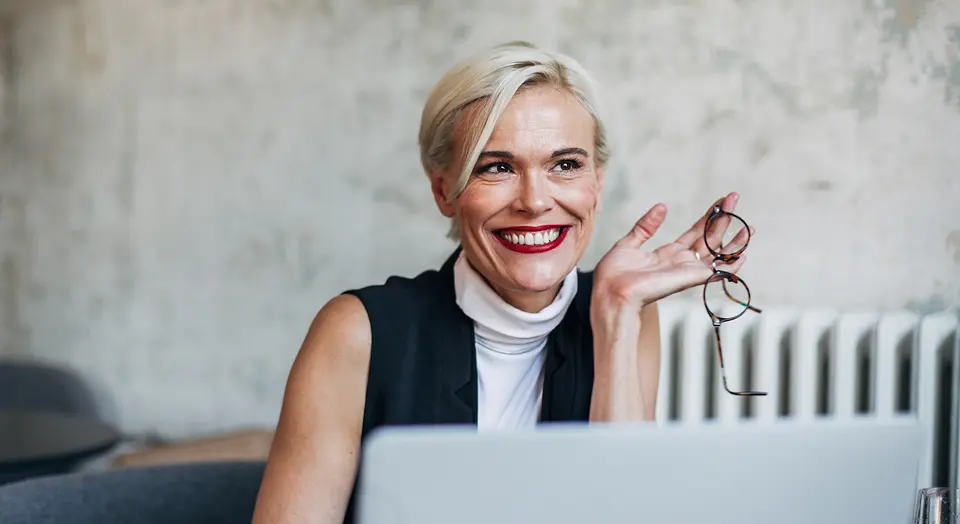Blonde Frau sitzt in einem Café am Laptop und schaut in die Ferne
