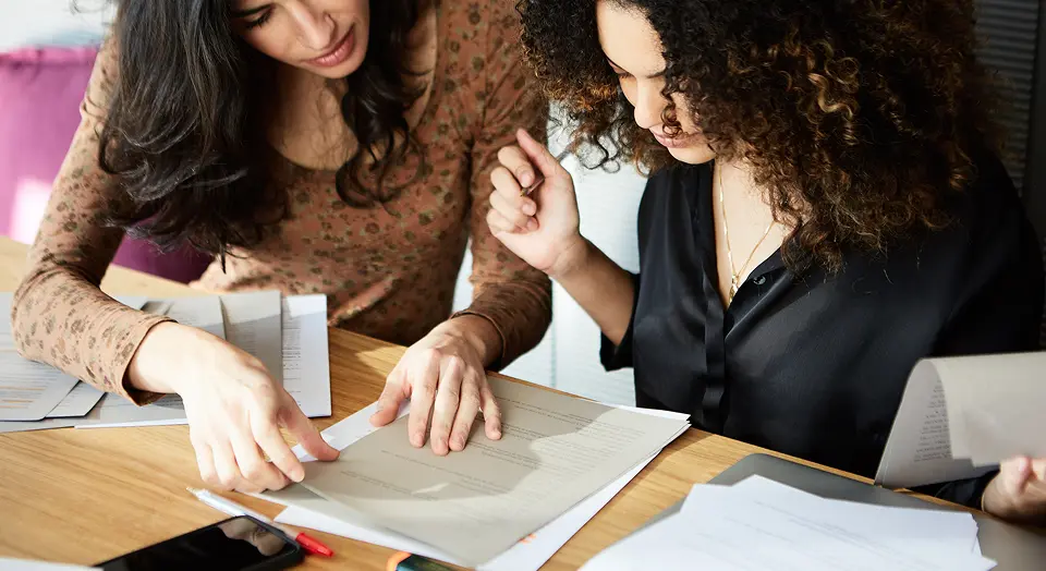 Zwei Frauen sitzen an einem Tisch und schauen sich gemeinsam Dokumente an