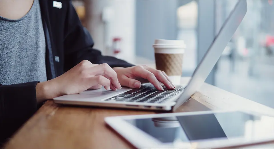 Nahaufnahme eines Mannes, der in einem Café an seinem Laptop arbeitet