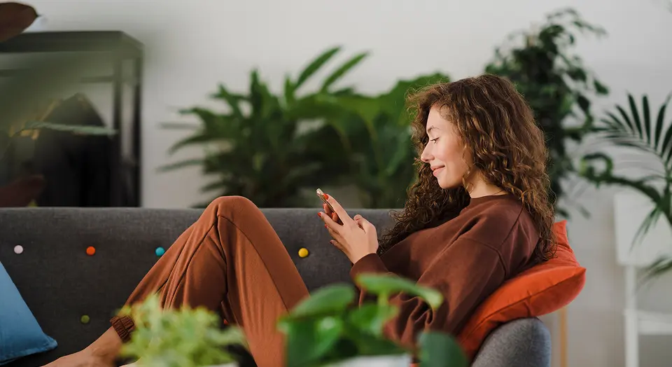 Lockige Frau liegt auf dem Sofa und schaut in ihr Smartphone