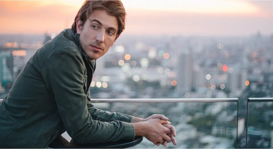 Mann in Sakko steht auf einer Dachterrasse und schaut in die Ferne