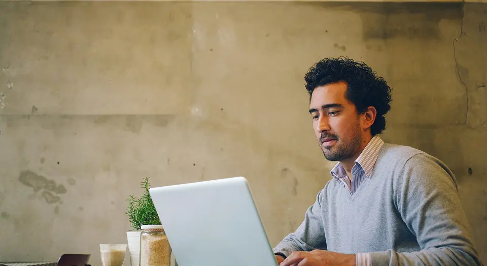 Dunkelhaariger Mann sitzt vor einer goldenen Wand an seinem Laptop