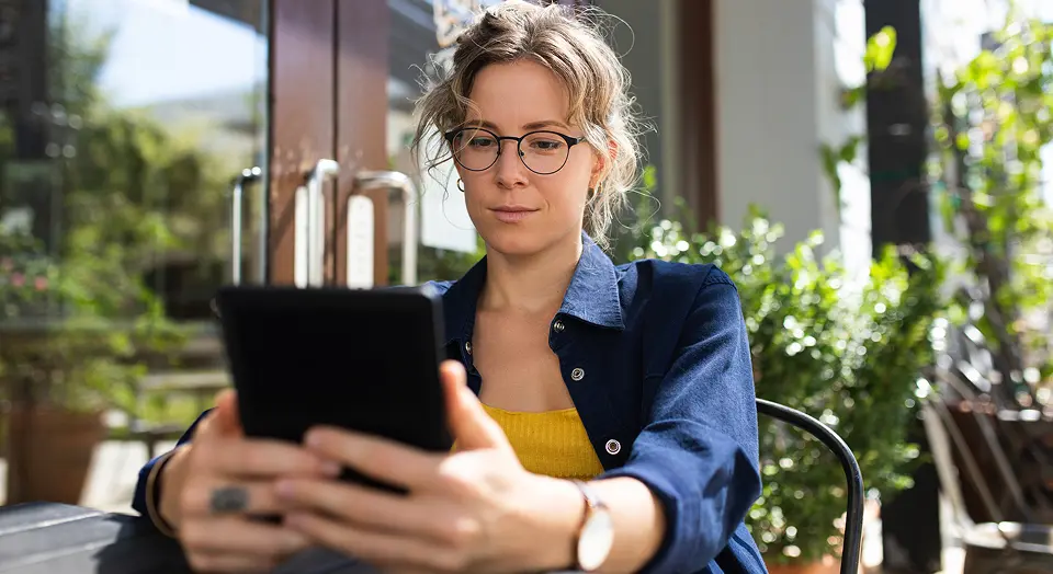 Frau mit Brille sitzt in einem grünen Café und schaut in ihr Tablet