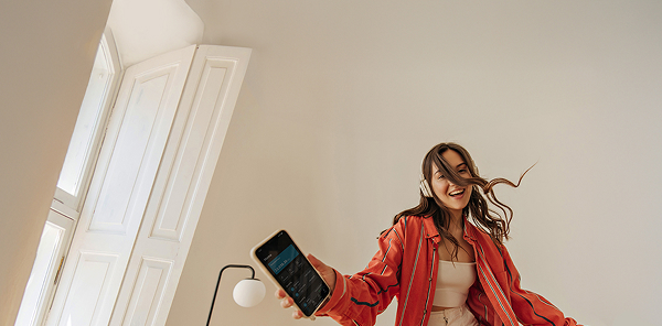 Mädchen mit brauen Haaren und orangenen Hemd hört Musik mit ihren Kopfhörern und hat ihr Smartphone in der Hand
