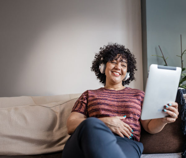 Frau mit schwarzen Locken liest lächelnd in ihrem Tablet