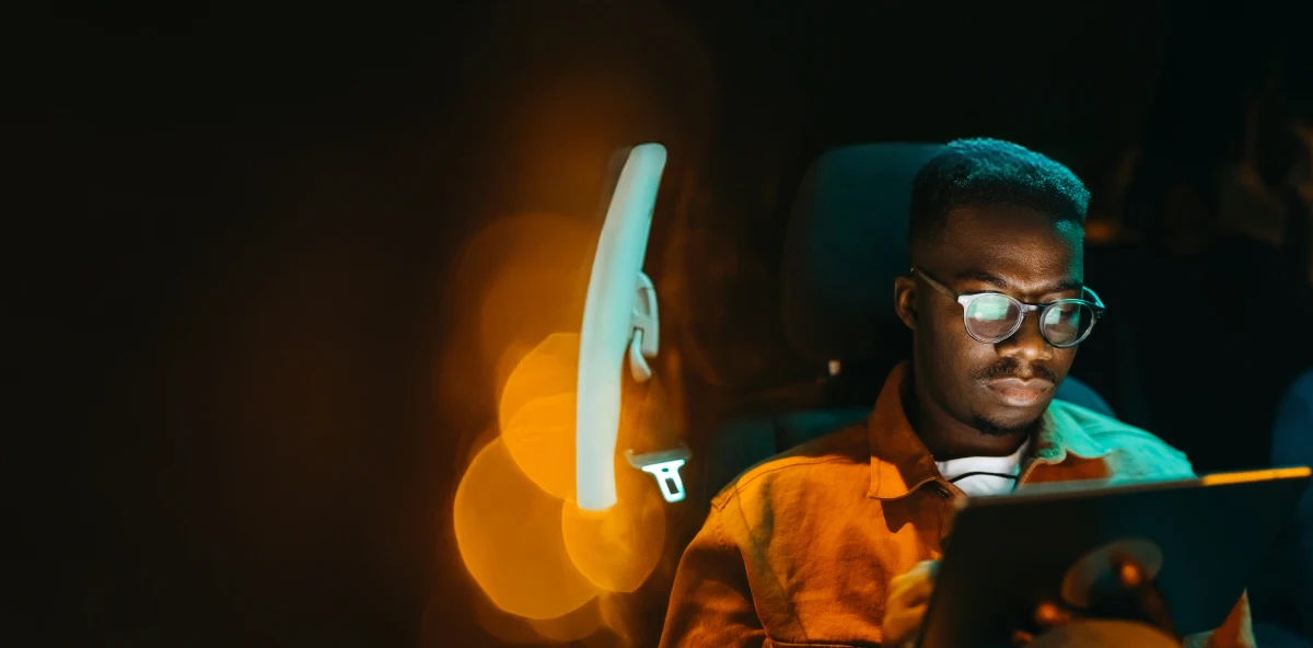 Mann mit Brille sitzt nachts im Auto und arbeitet an seinem Laptop, der sich in der Brille spiegelt