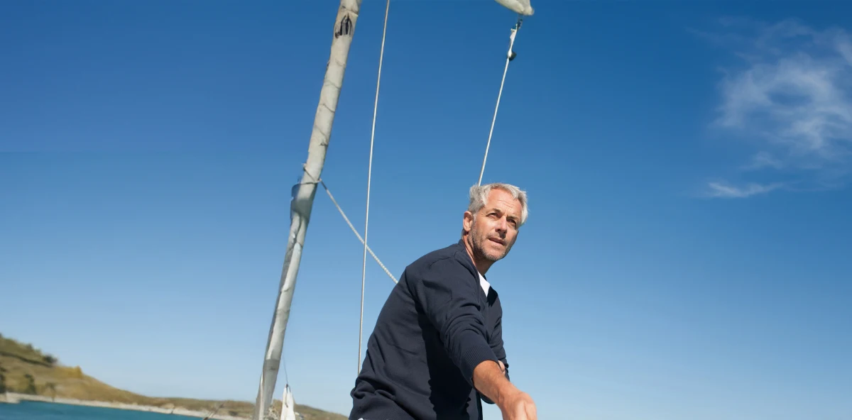 Mann mit grauen Haaren hisst auf einem Boot die Segel