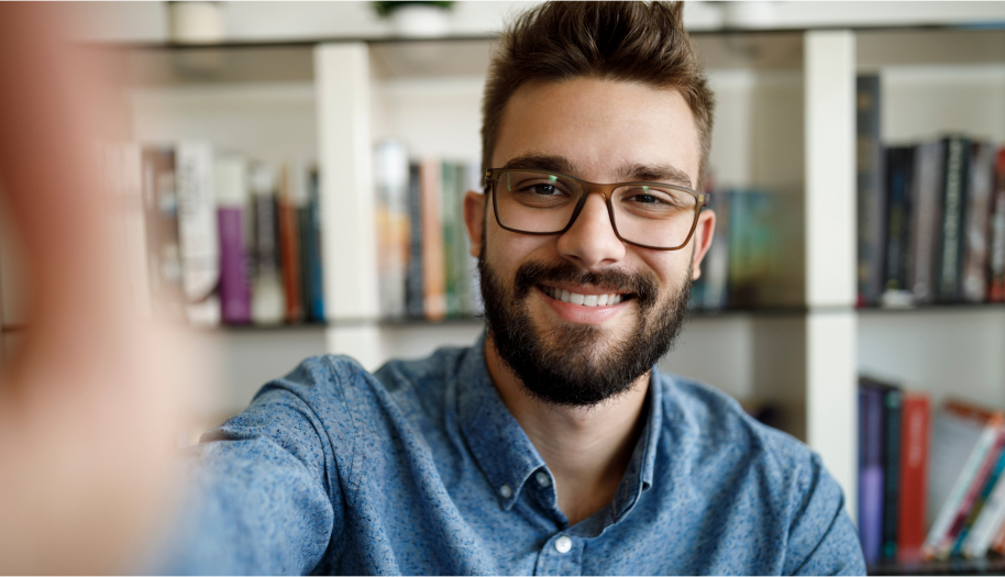 Dunkelhaariger Mann mit Brille in Jeanshemd macht ein Selfie von sich bei der Arbeit